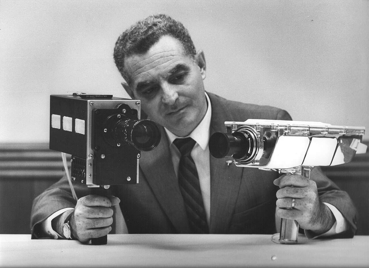 Stan Lebar displays a Westinghouse Apollo field-sequential color television camera alongside a monochrome camera.