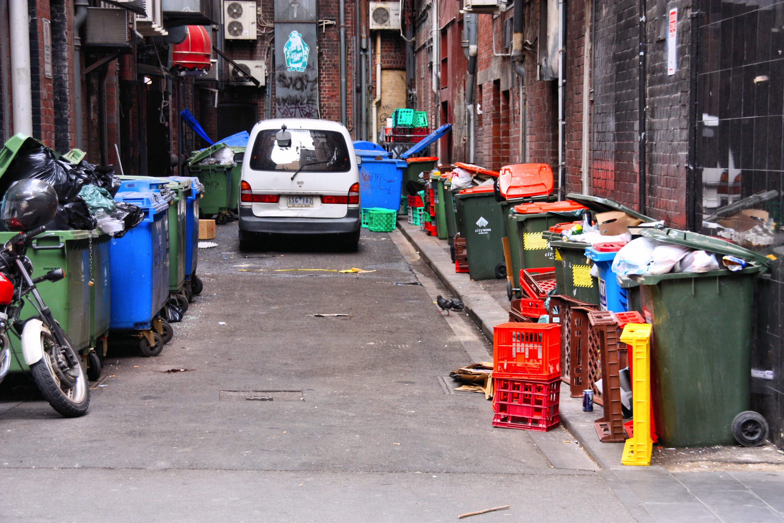 An urban alleyway lined with restaurant trash and recycling bins.