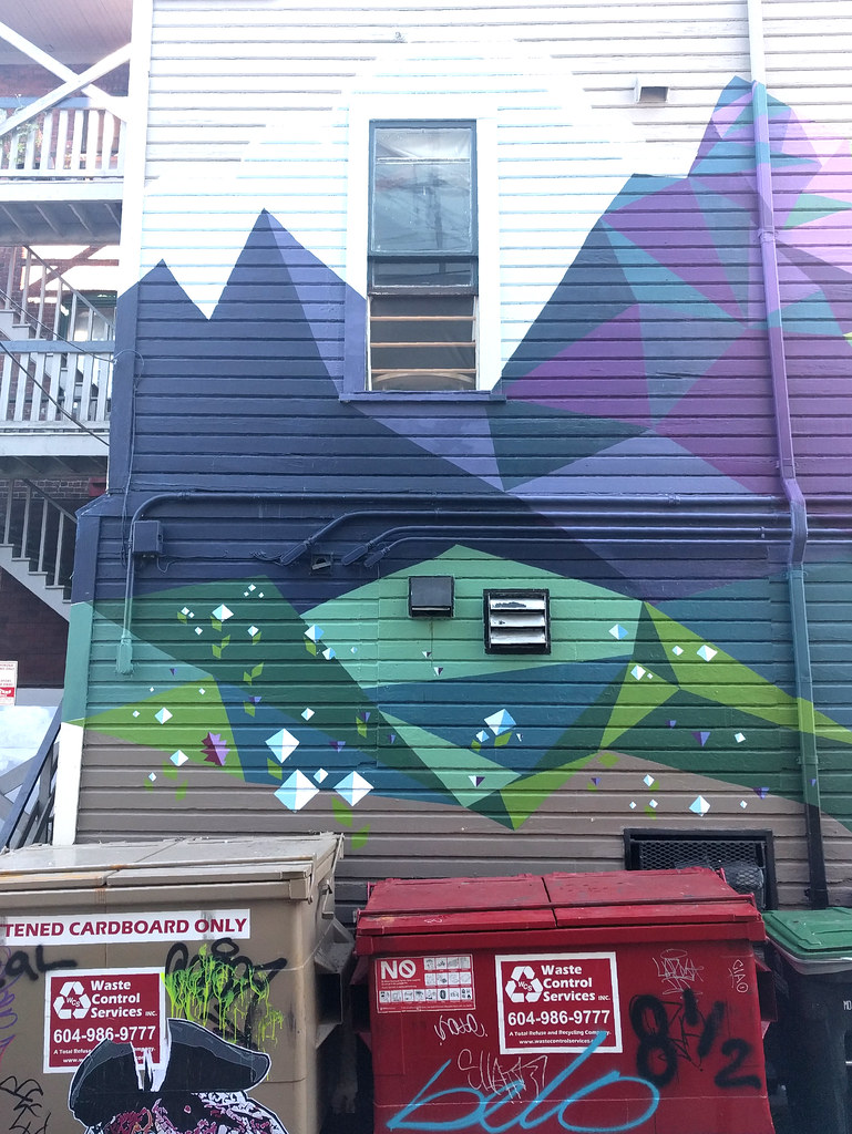 Waste bins positioned beneath an alley mural.