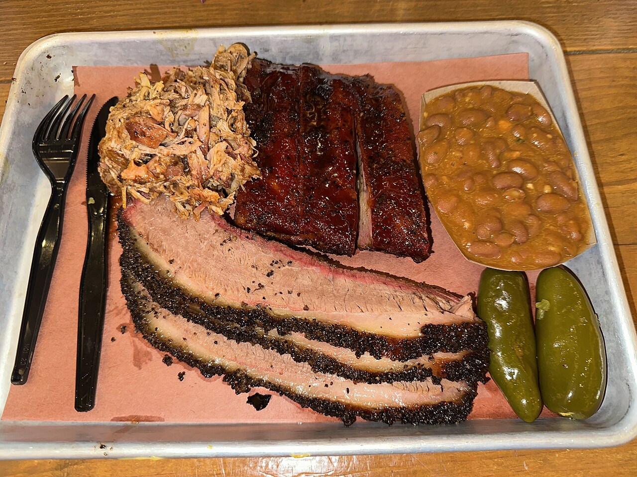 A barbecue tray with sliced brisket, ribs, pulled pork, and beans.